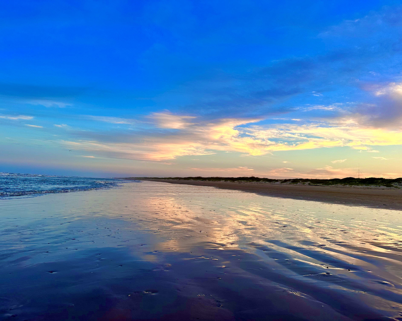color photograph of a beach at sunset with the sky reflected in the incoming waves