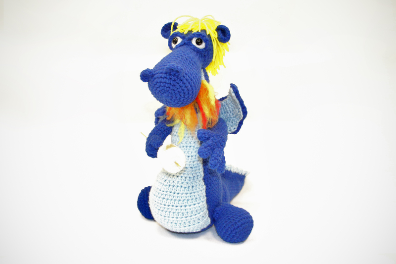 Crochet figure of a blue dragon. The dragon has yellow hair and is breathing fire to roast a marshmallow on a stick.