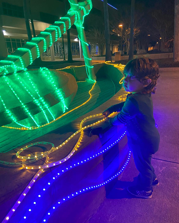 Color photograph taken at night of a small child looking at bright lights on an outdoor sculpture