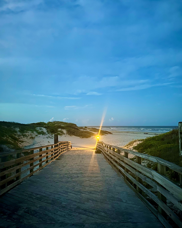 color photograph of a lamp at the end of a wooden walkway leading out of sand dunes onto the shoreline