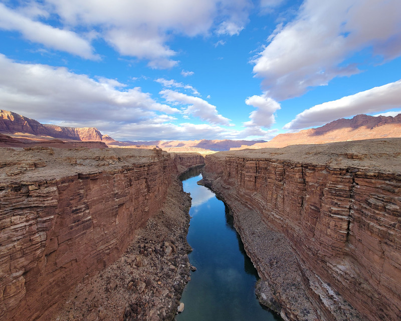 color photograph of a canyon with a river reflecting the clouded sky