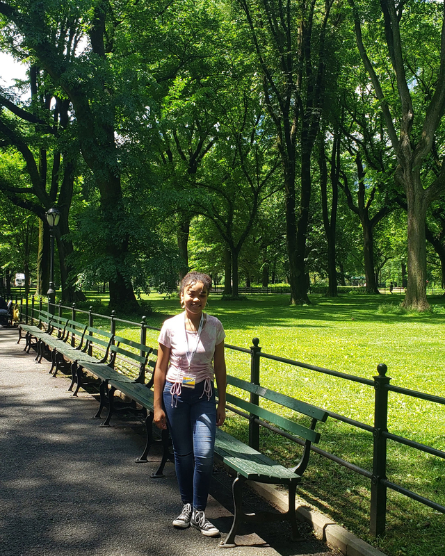 color photograph of a figure standing near benches and a fence in a wooded park