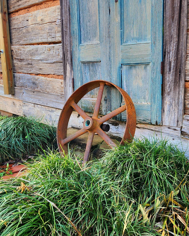 color photograph of a rusted wheel leaning against the outside of a building