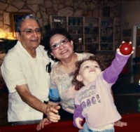 Arturo and Marie Vasquez with their granddaughter, who is on the family pool table  holding a cue ball.